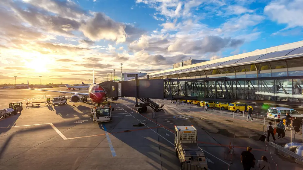 A passenger plane parked at an airport gate for boarding passengers with a colorful sunset in the background