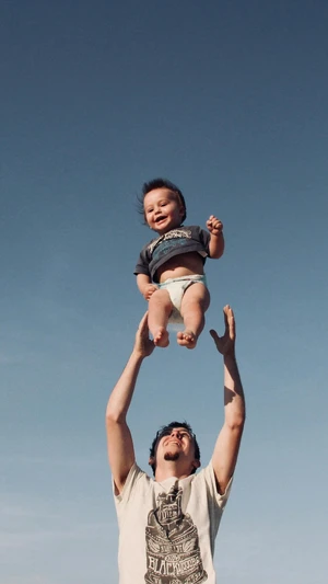 Dad tossing his toddler in the air over his head.