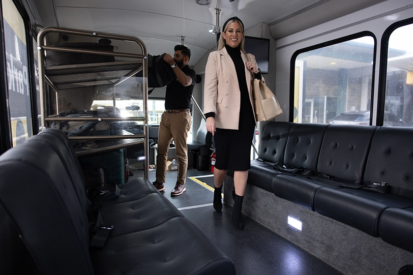 A woman boards an airport shuttle while the driver loads her bag.