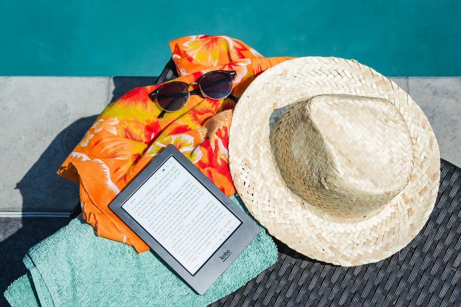 sunglasses and hat with an e-reader by the pool 